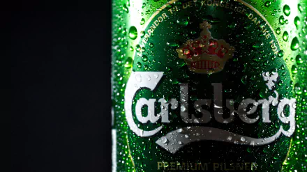 Close-up 4K Ultra HD image of a chilled Carlsberg beer bottle with water droplets on the green glass, set against a dark background.