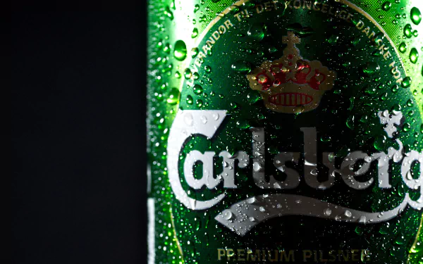 Close-up 4K Ultra HD image of a chilled Carlsberg beer bottle with water droplets on the green glass, set against a dark background.