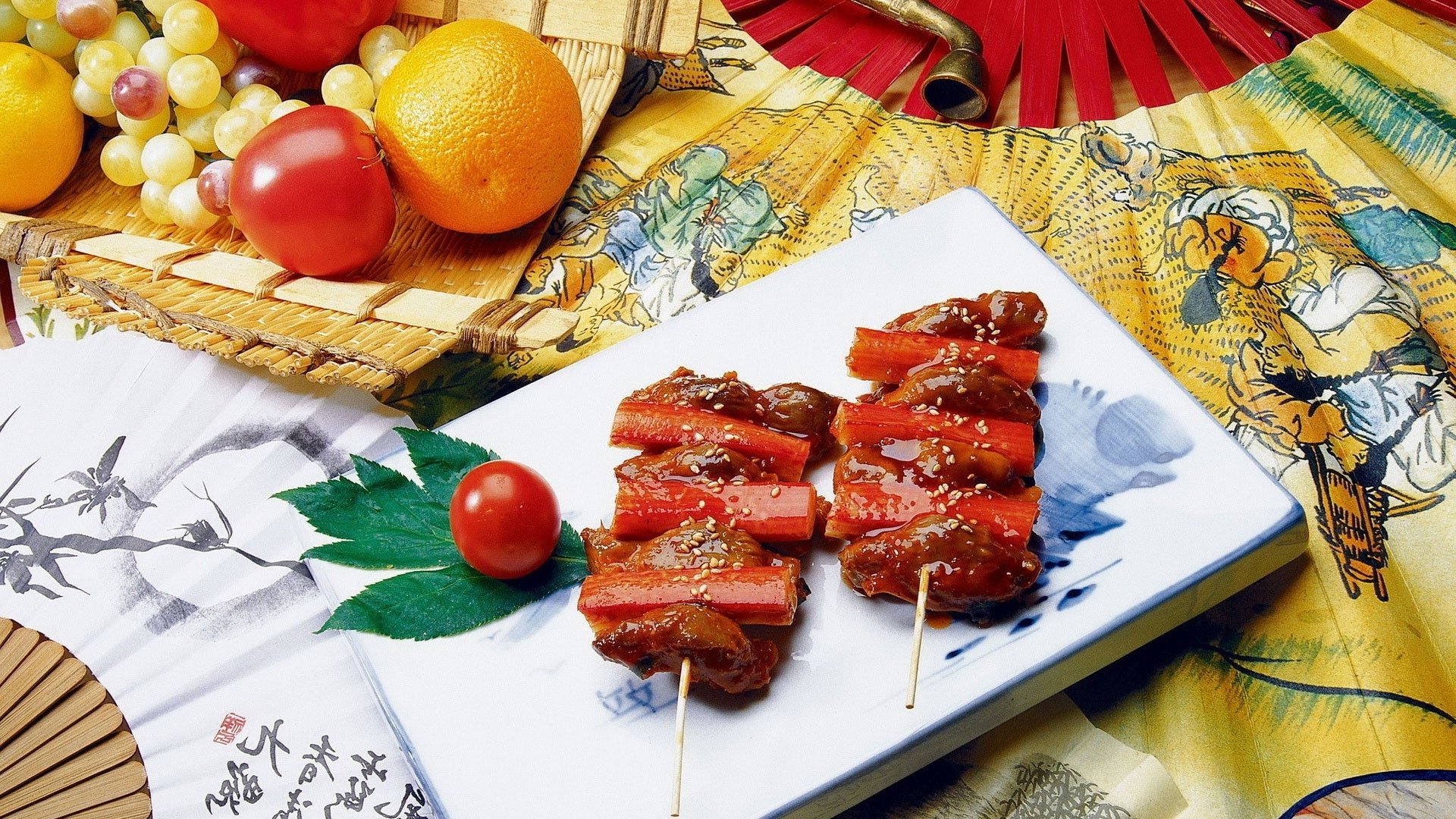 HD desktop wallpaper of Japanese food: glazed crab-meat skewers on a plate with cherry tomato, grapes and lemon, set on a patterned cloth with a decorative fan.