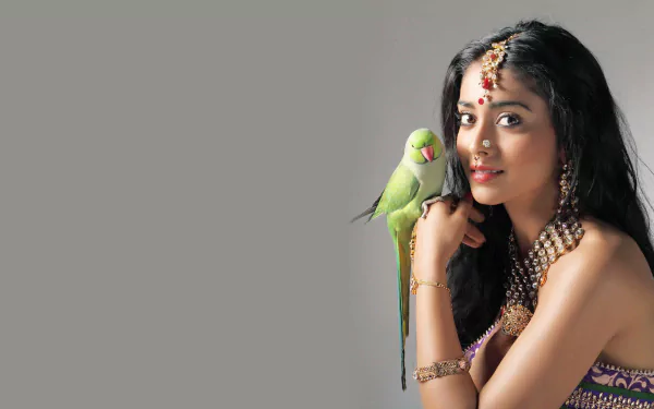 A captivating HD wallpaper featuring celebrity Shriya Saran with a green parrot, showcasing elegance and charm against a soft, neutral background.