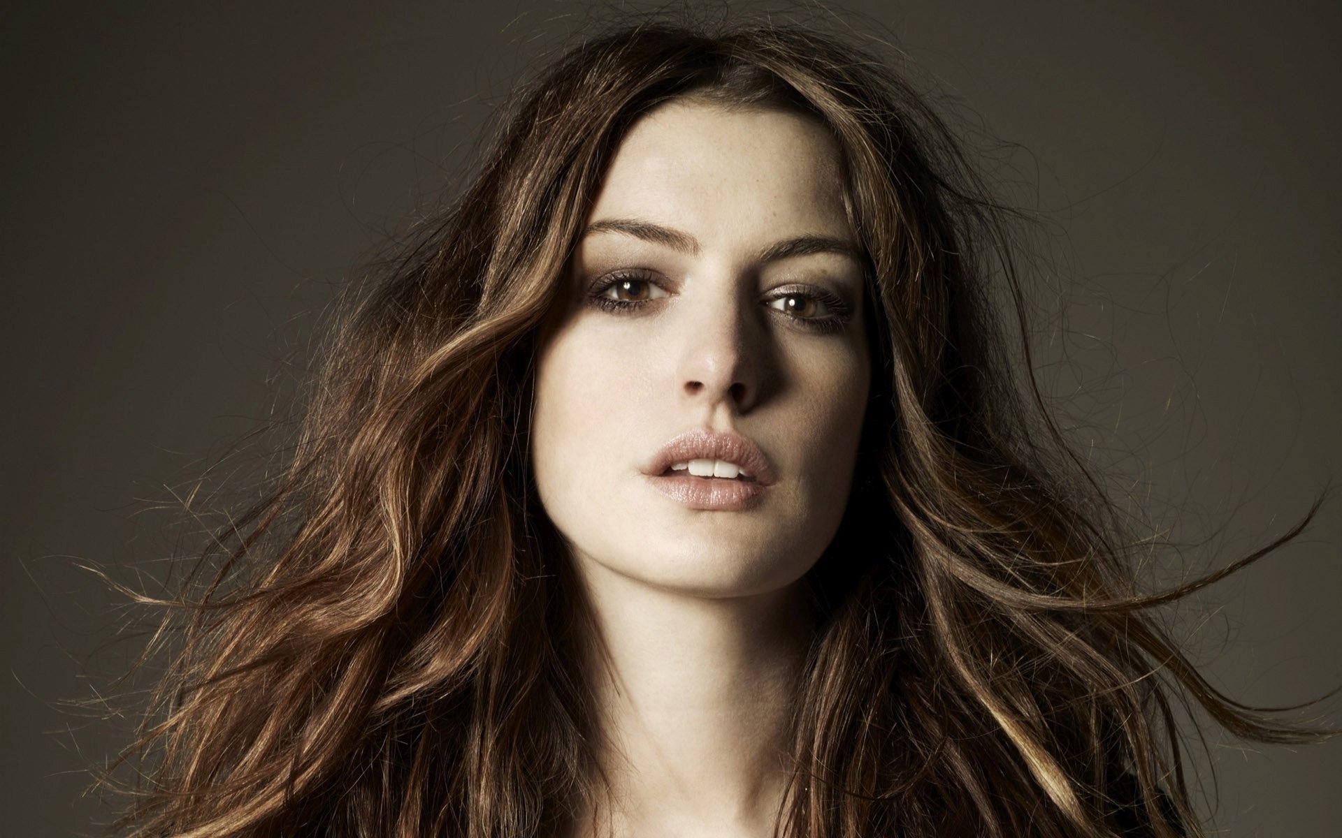 HD desktop wallpaper featuring a close-up of Anne Hathaway’s face with flowing hair against a neutral background.