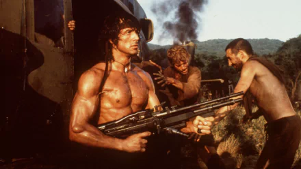 HD wallpaper featuring a scene from Rambo: First Blood Part II, showcasing an intense moment with the iconic character holding a weapon amidst fellow soldiers.