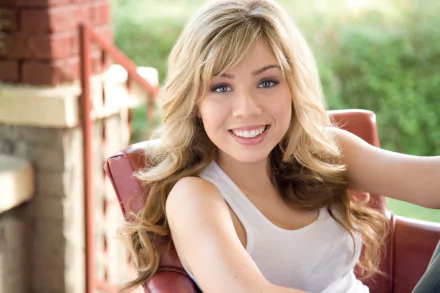 Blonde actress Jennette McCurdy smiles warmly while seated outdoors, featured in an HD PC desktop wallpaper background.