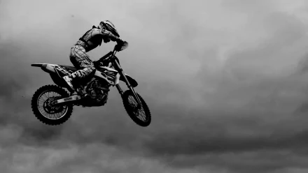 A motocross rider performs an impressive jump against a dramatic cloudy background, capturing the thrill of the sport in this HD desktop wallpaper.