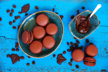 5K Ultra HD PC desktop wallpaper of chocolate macarons in a ceramic bowl with chocolate spread and scattered coffee beans on a bright turquoise wooden background.