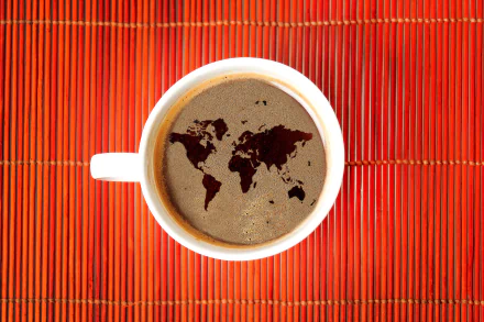 A top view of a cappuccino featuring a world map design in the foam, set against a vibrant red background. This stunning 4K Ultra HD image showcases a unique coffee presentation.