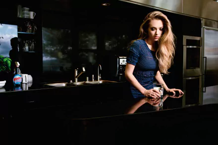 HD PC desktop wallpaper featuring celebrity Amanda Seyfried leaning on a modern kitchen counter with a reflective black surface and dark cabinetry in the background.