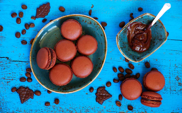 5K Ultra HD PC desktop wallpaper of chocolate macarons in a ceramic bowl with chocolate spread and scattered coffee beans on a bright turquoise wooden background.