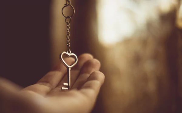 Photography: outstretched hand holding a dangling heart-shaped key against a warm, blurred bokeh — HD PC desktop wallpaper and background.