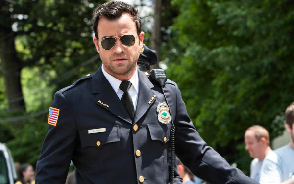HD PC desktop wallpaper/background showing a uniformed police officer from the TV show The Leftovers walking outdoors on a sunlit suburban street.