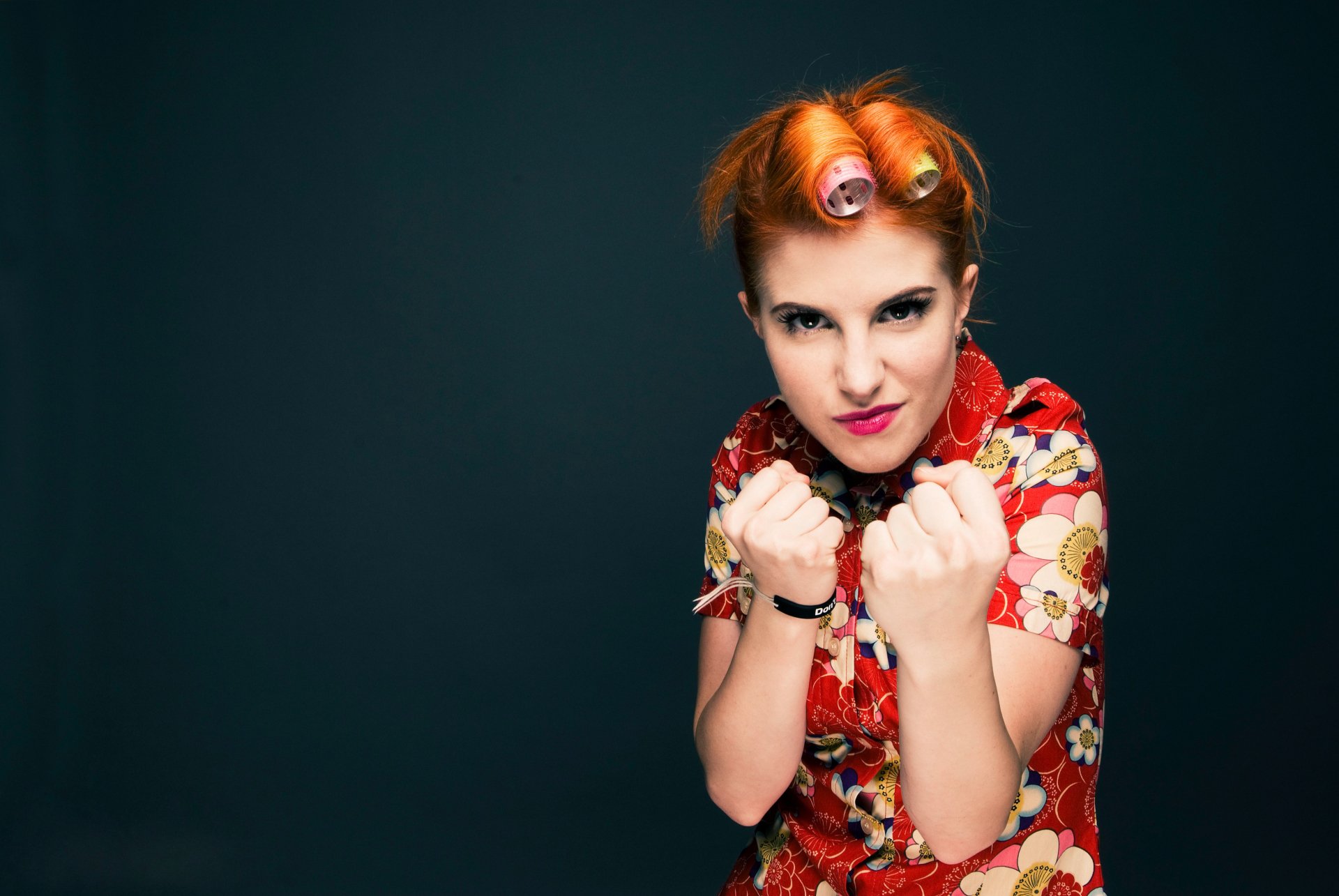 2K Quad HD PC wallpaper of a music singer with bright orange hair in curlers and a floral blouse, fists raised against a dark background.