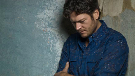 HD PC desktop wallpaper of a pensive country music singer in a blue shirt leaning against a textured wall, moody portrait-style background.