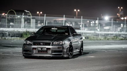 A Nissan Skyline R34 is parked in a dimly lit area, showcasing its sleek design and bold presence against an urban backdrop, making it an impressive HD desktop wallpaper.