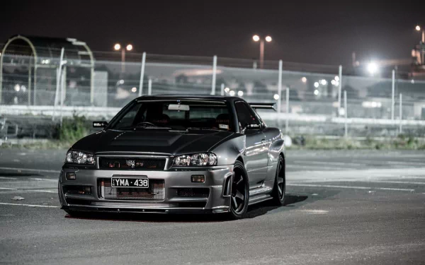 A Nissan Skyline R34 is parked in a dimly lit area, showcasing its sleek design and bold presence against an urban backdrop, making it an impressive HD desktop wallpaper.