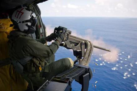 A soldier operating a machine gun from a helicopter, overlooking the ocean. This high-definition image serves as a striking desktop wallpaper and background.