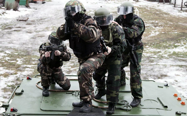Military HD PC desktop wallpaper: four camouflaged soldiers in full combat gear and helmets on an armored vehicle, aiming rifles over snowy ground.