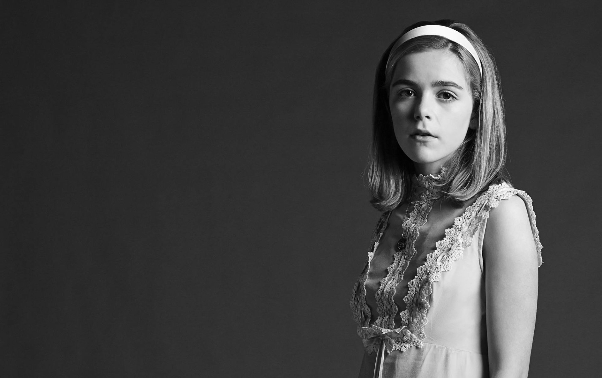 Black-and-white HD desktop wallpaper of a young female celebrity in a headband and lace dress, standing and gazing at the camera against a plain dark background.