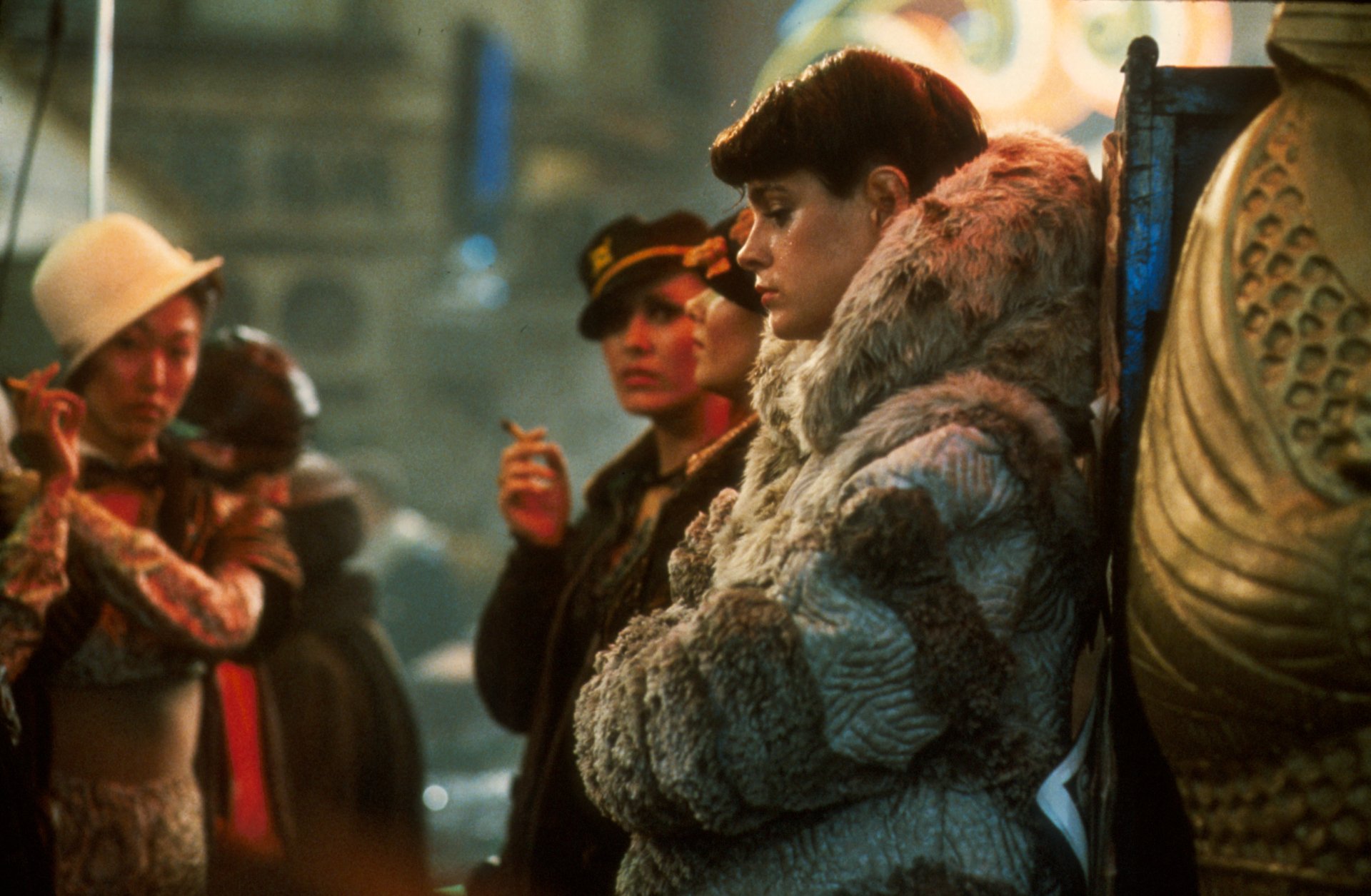 Blade Runner 2K Quad HD PC desktop wallpaper — neon-lit street crowd; a fur-coated woman leans against a column while others smoke.