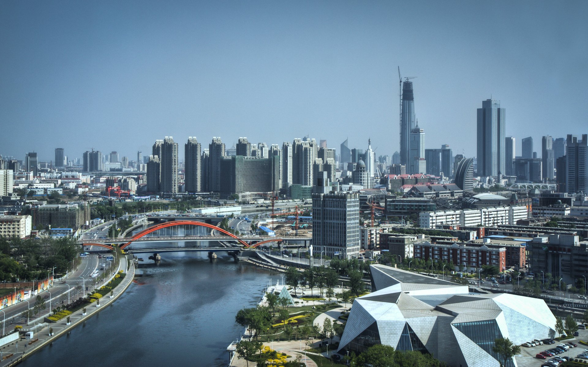 HD desktop wallpaper showing the modern cityscape of Tianjin, China, featuring a river, bridges, and high-rise buildings under a clear sky.