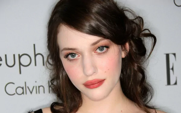 HD desktop wallpaper featuring celebrity Kat Dennings with soft makeup and wavy dark hair against a branded event backdrop.