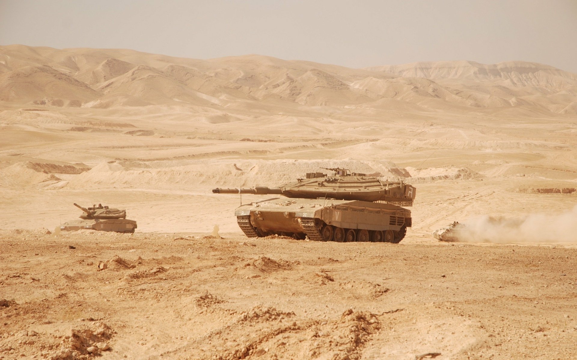 2K Quad HD PC desktop wallpaper showing Merkava main battle tanks traversing a dusty desert landscape, dust clouds trailing behind them.