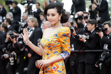 A stunning silk dress adorned actress Fan Bingbing waves gracefully amidst photographers, capturing attention at a glamorous event. A vibrant display of elegance in 4K Ultra HD.