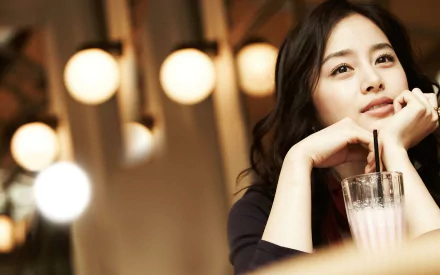 A Korean celebrity is enjoying a cocktail, resting her chin on her hands with a thoughtful expression, surrounded by soft, glowing lights in this elegant HD desktop wallpaper.