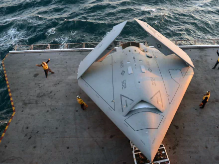 Top-down view of a Northrop Grumman X-47B unmanned military aircraft on an aircraft carrier deck with crew, 2K Quad HD PC desktop wallpaper and background.