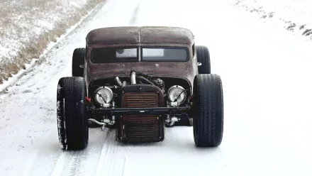 A vintage rat rod parked on a snowy road, showcasing its rustic design and powerful stance, captured as a high-definition desktop wallpaper and background.