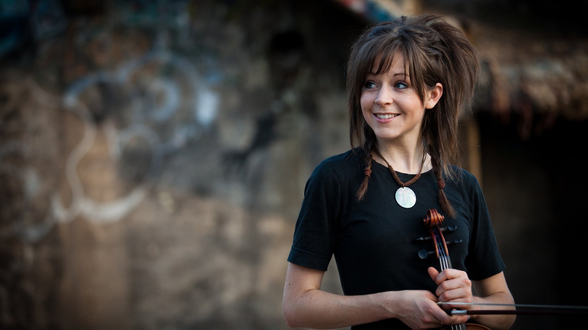 A vibrant HD wallpaper featuring Lindsey Stirling, smiling while holding her violin against a rustic background, capturing the essence of music and artistry.