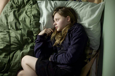 Chloë Grace Moretz lies contemplatively on a bed, captured in a still from the movie *Let Me In*. This HD desktop wallpaper evokes a sense of introspection and moodiness.