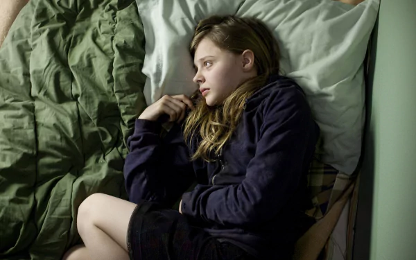 Chloë Grace Moretz lies contemplatively on a bed, captured in a still from the movie *Let Me In*. This HD desktop wallpaper evokes a sense of introspection and moodiness.