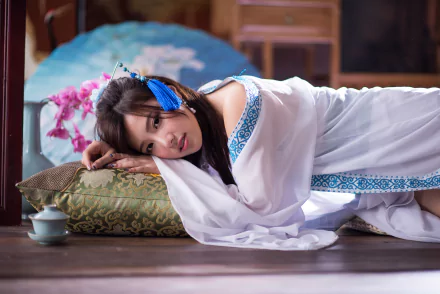 A Taiwanese woman in traditional attire relaxes on a cushion surrounded by orchids and a decorative vase, creating a serene atmosphere in this HD desktop wallpaper.