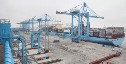 A container ship at a busy port, surrounded by large blue cranes and stacked shipping containers, depicted in a detailed 4K Ultra HD desktop wallpaper.