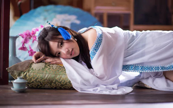 A Taiwanese woman in traditional attire relaxes on a cushion surrounded by orchids and a decorative vase, creating a serene atmosphere in this HD desktop wallpaper.