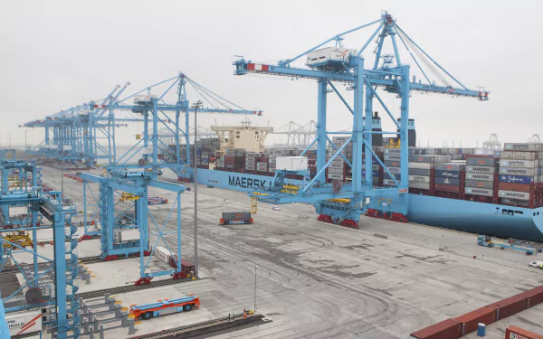 A container ship at a busy port, surrounded by large blue cranes and stacked shipping containers, depicted in a detailed 4K Ultra HD desktop wallpaper.