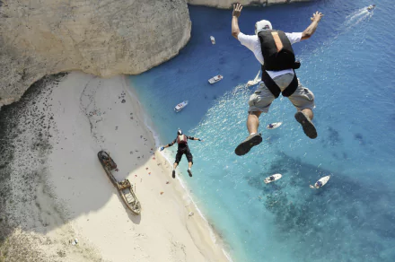 Two skydivers leap from a height, surrounded by a stunning blue ocean and a sandy beach below. A breathtaking sports moment captured in an HD wallpaper.