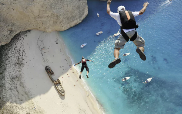 Two skydivers leap from a height, surrounded by a stunning blue ocean and a sandy beach below. A breathtaking sports moment captured in an HD wallpaper.
