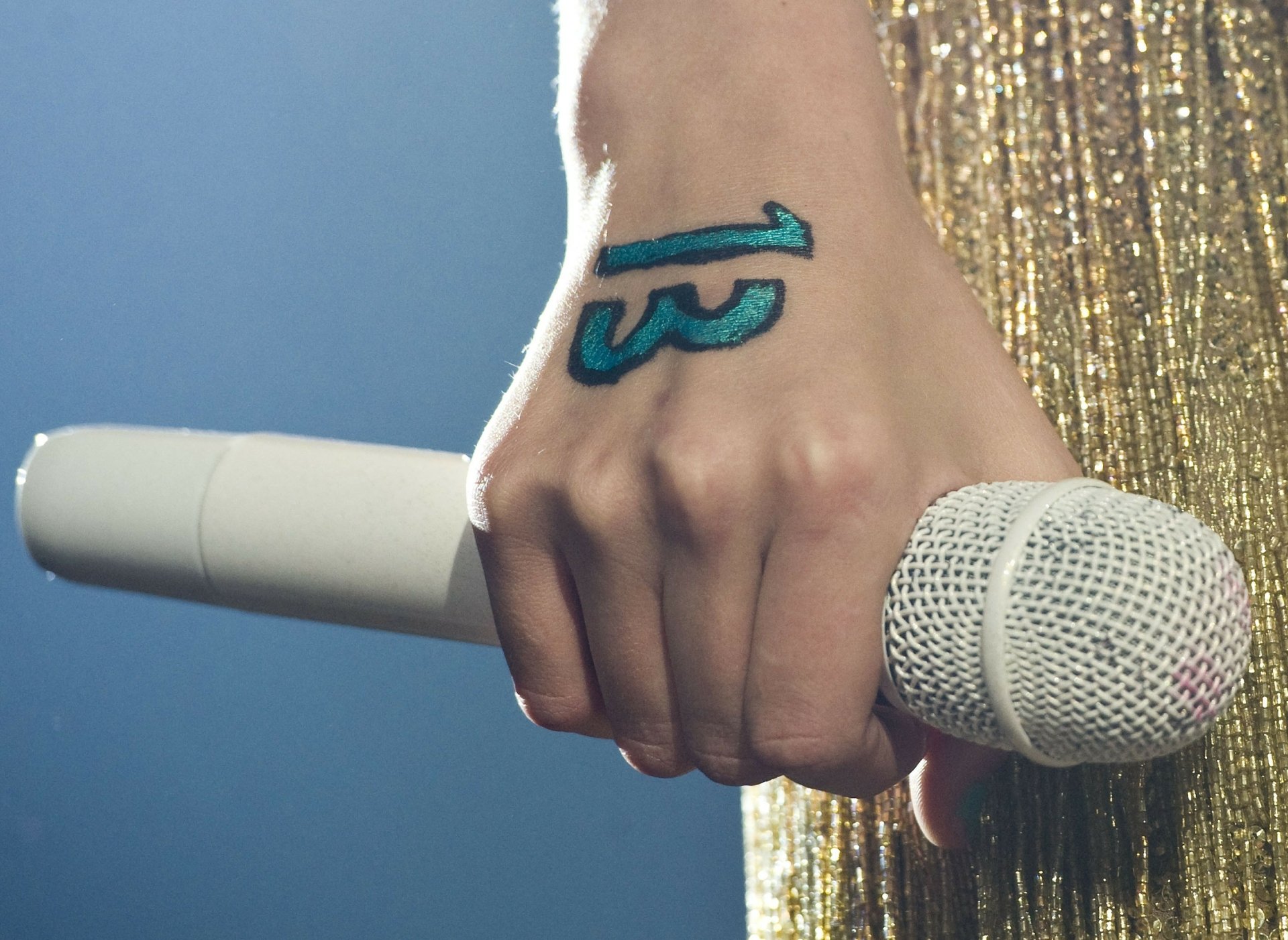 Close-up of a hand holding a white microphone with the number 13 written on it, set against a blue background, featured in a Taylor Swift HD PC desktop wallpaper.