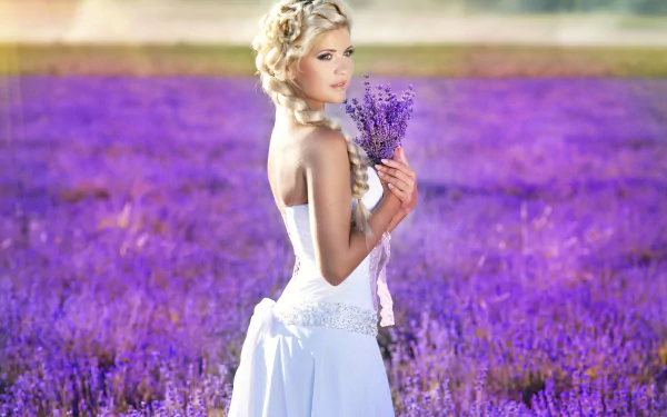 A bride in a wedding dress stands in a lavender field, holding a bouquet of lavender flowers. Her hair is styled in a plait. The image is a high-definition desktop wallpaper and background.