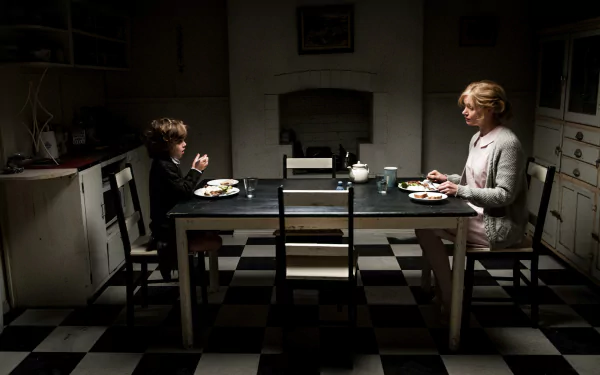 Essie Davis and Noah Wiseman share a tense dinner scene from the movie The Babadook, captured in a 4K Ultra HD PC desktop wallpaper and background.