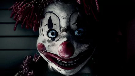 Close-up of a cracked, sinister clown doll with chipped paint, red nose and glassy blue eyes — Poltergeist (2015) movie HD PC desktop wallpaper/background.