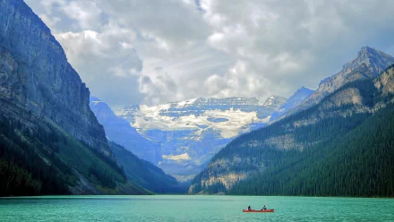 A serene view of Lake Louise in Banff National Park, Alberta, Canada, featuring a boat on turquoise water with Fairview Mountain and snowy peaks in the background.