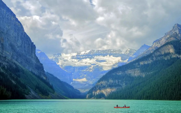 A serene view of Lake Louise in Banff National Park, Alberta, Canada, featuring a boat on turquoise water with Fairview Mountain and snowy peaks in the background.
