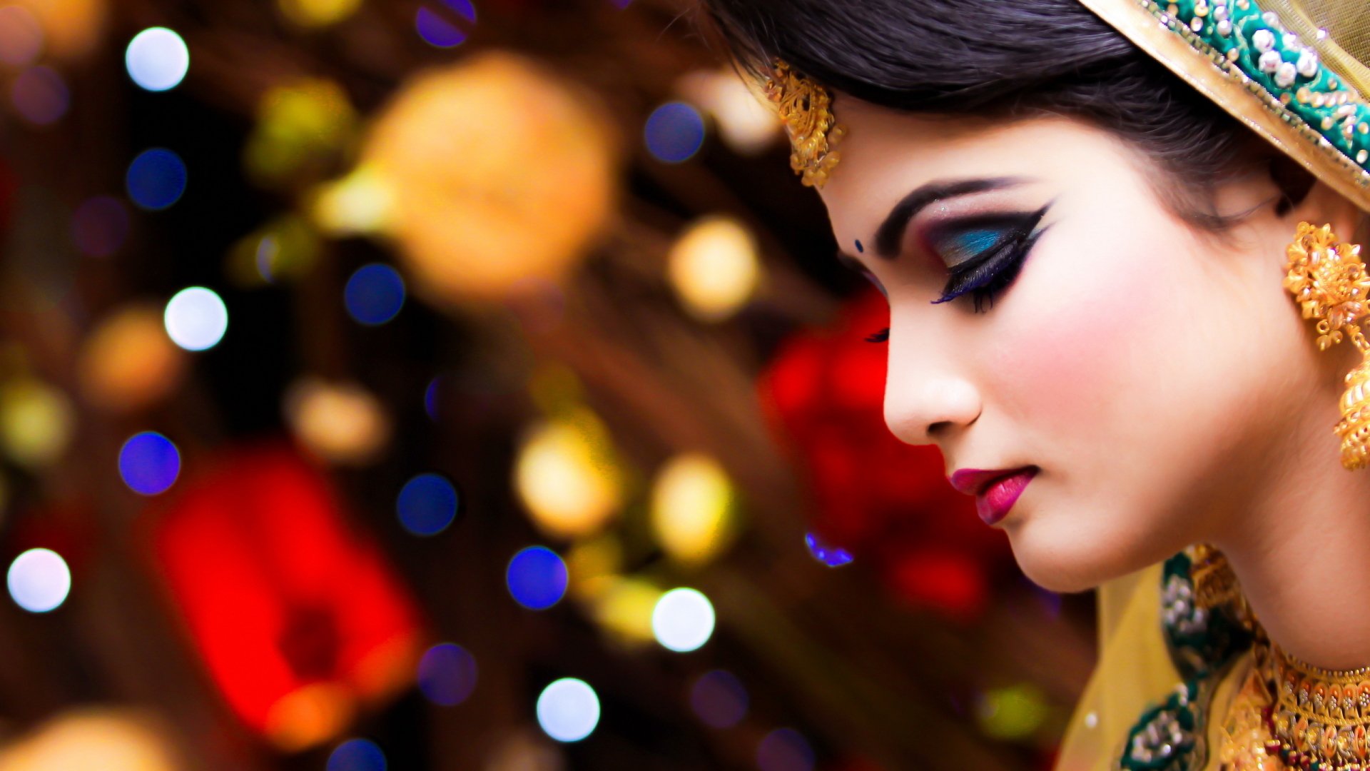 A stunning Indonesian bride with intricate makeup is captured in profile against a vibrant bokeh background, creating a captivating HD wallpaper for desktop use.
