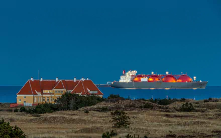 HD desktop wallpaper showing a tanker vessel illuminated at night near a coastal house under a clear blue sky.