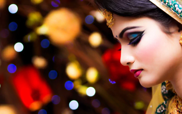 A stunning Indonesian bride with intricate makeup is captured in profile against a vibrant bokeh background, creating a captivating HD wallpaper for desktop use.
