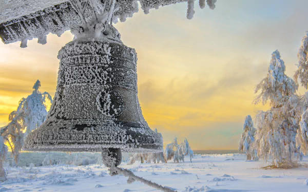 Frost-coated man-made bell hanging over a snow-covered field at sunrise, composed as a 2K Quad HD PC desktop wallpaper and background.