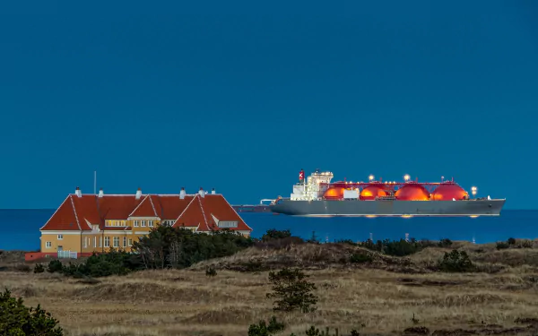 HD desktop wallpaper showing a tanker vessel illuminated at night near a coastal house under a clear blue sky.