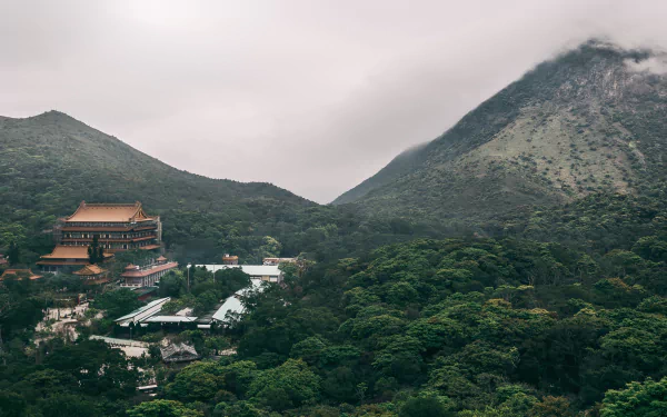 Fog blankets the mountainous landscape of Lantau Island, Hong Kong, featuring the serene Po Lin Monastery nestled among lush greenery.